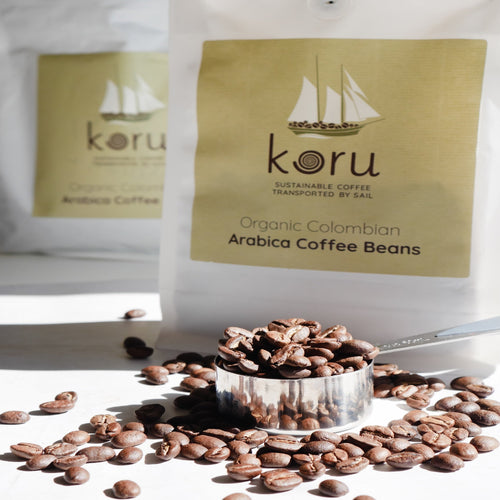 Koru Organic Colombian Arabica Coffee Beans with coffee beans scattered around on a light background